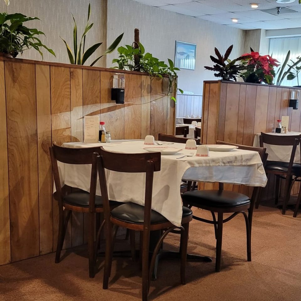 A dining table set for two with white tablecloths and dark wooden chairs in Lai Lai Restaurant.