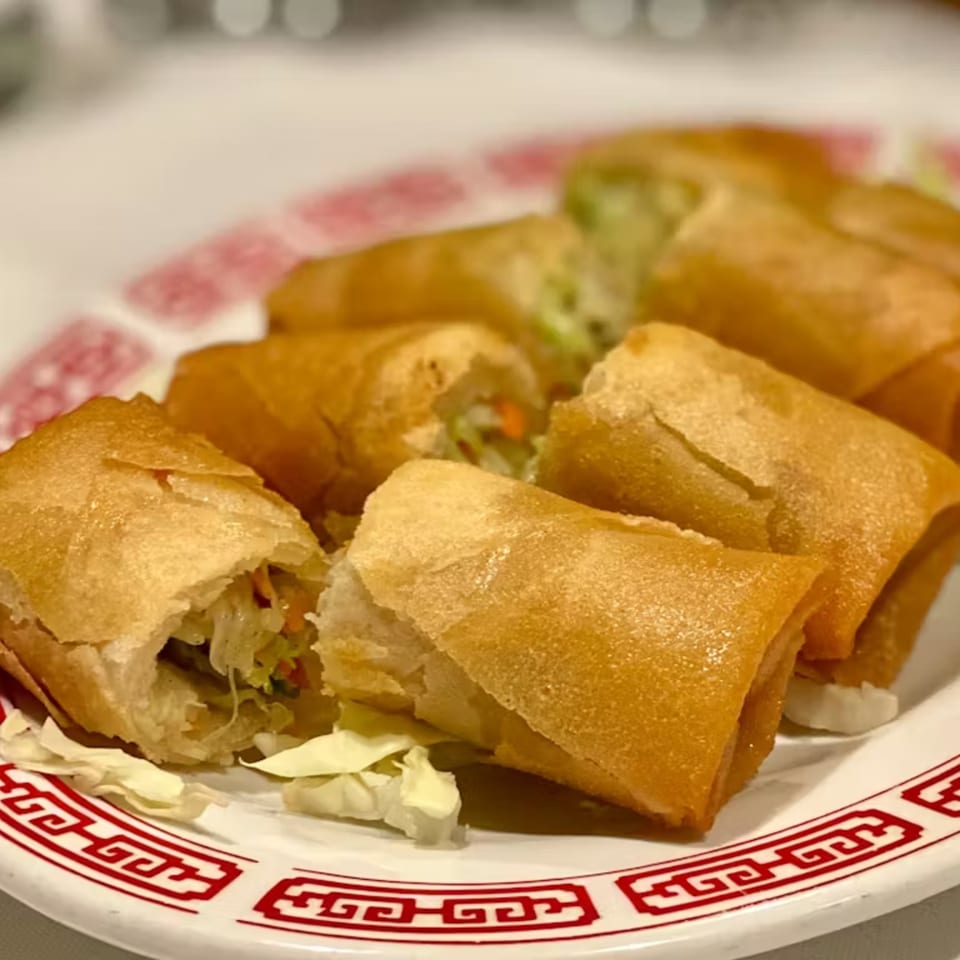 Golden-brown Lai Lai Restaurant egg rolls, one cut open to show the vegetable filling, on a white plate.