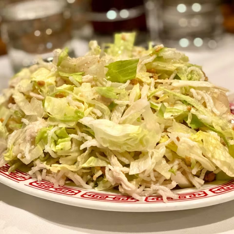A large serving of shredded lettuce and crispy noodles on a white plate with a red border.