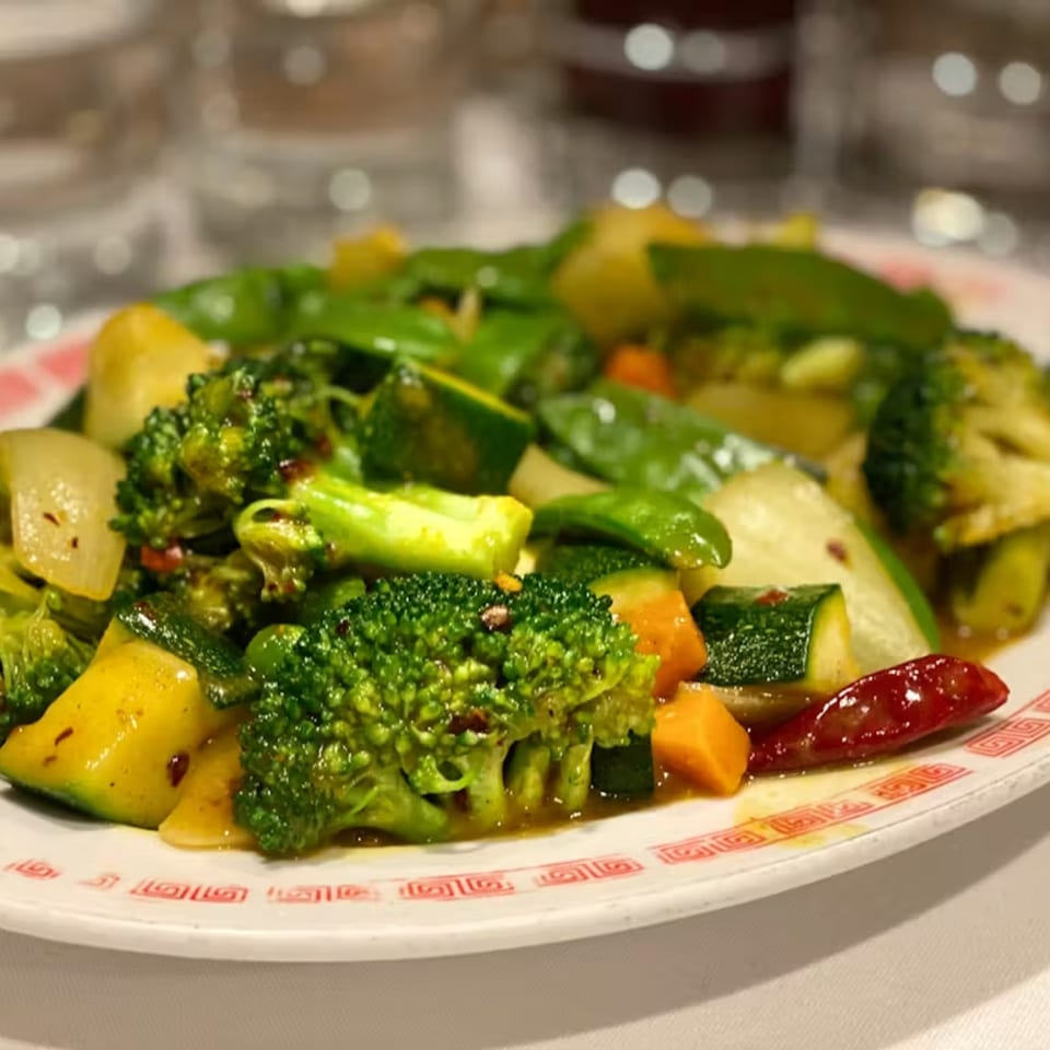 A vibrant Chinese stir-fry with broccoli, zucchini, carrots, and snow peas on a white plate.