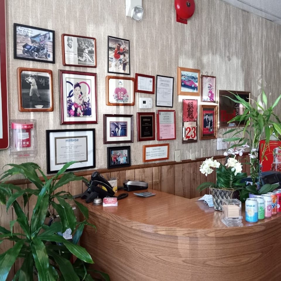 A wooden reception desk with plants, drinks, and framed photos and awards on the wall.
