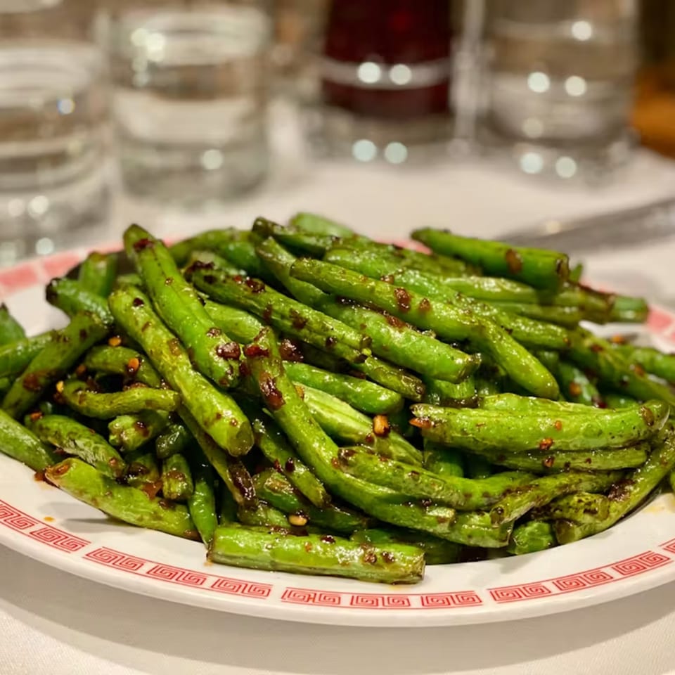A white plate with a red border filled with stir-fried green beans, seasoned with chili flakes.